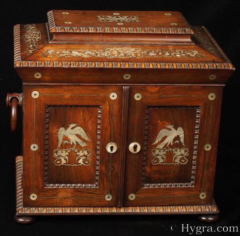 William IV fully fitted figured rosewood  table cabinet of architectural form inlaid with mother of pearl depicting stylized flowers and on the doors  perched birds of prey .  The top compartment is fitted for sewing and retains its mother of pearl topped spools and tools. The doors which have fielded panels framed with turned gadrooning. Inside they have embossed maroon Morocco leather, Behind the doors there are three drawers with turned mother of pearl handles and accents. The bottom drawer is a writing box; the middle is fitted for jewelry and has a lift out tray. The top is empty and lined with yellow paper.  Circa 1835.  Enlarge Picture